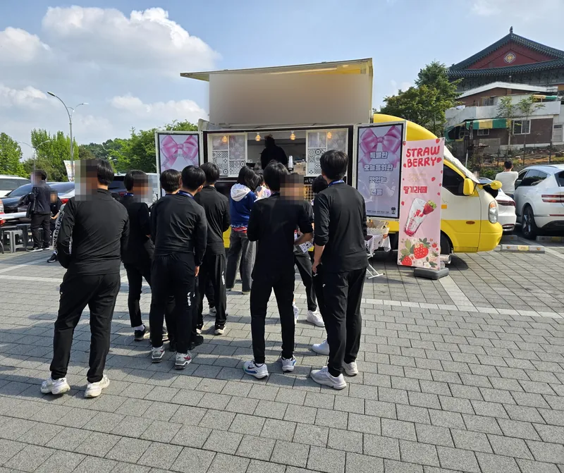 노란 커피 트럭 앞에 줄 선 운동복 차림의 선수들