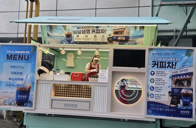 기업 응원 현수막을 단 민트색 커피투어트럭에서 직원이 음료를 준비하는 모습