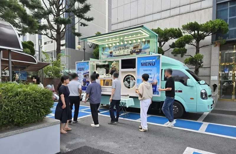 회사 건물 앞 민트색 트럭 주변에 모여 음료를 받는 직장인들